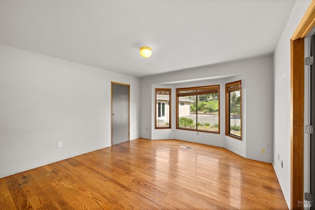 unfurnished room featuring light wood-type flooring, visible vents, and baseboards