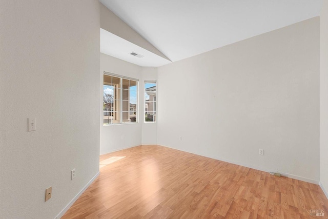 spare room with visible vents, light wood-type flooring, and vaulted ceiling