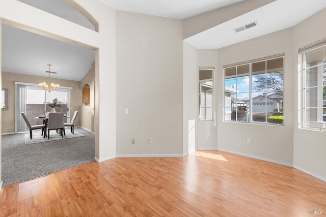 unfurnished room featuring an inviting chandelier, light wood-style flooring, a healthy amount of sunlight, and visible vents