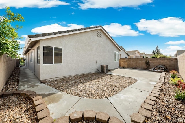 rear view of house featuring a patio area, stucco siding, central AC, and a fenced backyard