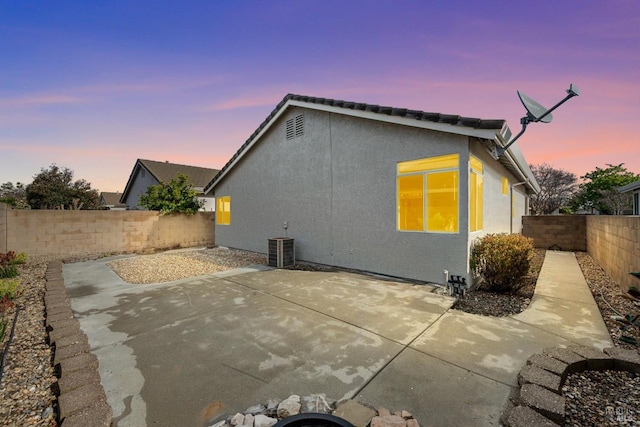 back of property at dusk featuring stucco siding, central AC, a fenced backyard, and a patio area