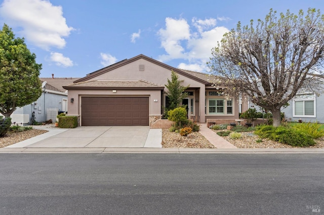 ranch-style home with an attached garage, a tile roof, driveway, stone siding, and stucco siding