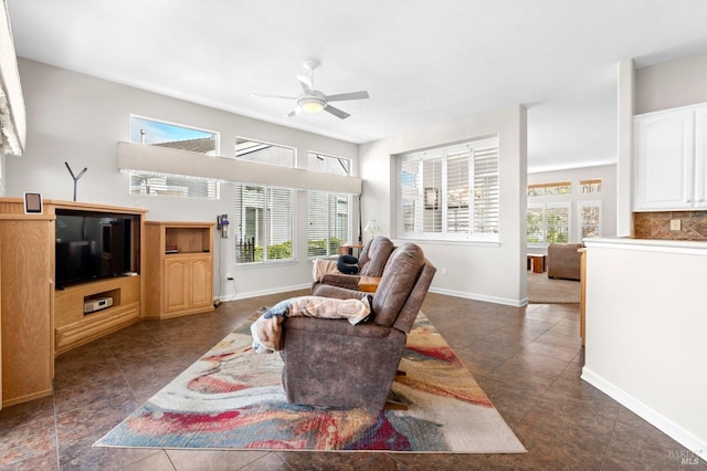 living area with a ceiling fan, dark tile patterned floors, and baseboards