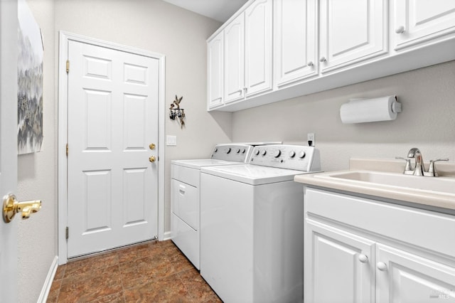 laundry room featuring cabinet space, baseboards, stone finish flooring, washing machine and dryer, and a sink