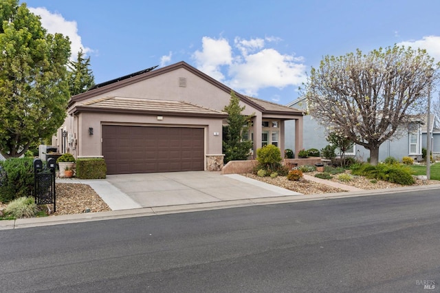 single story home featuring stucco siding, solar panels, concrete driveway, a garage, and stone siding