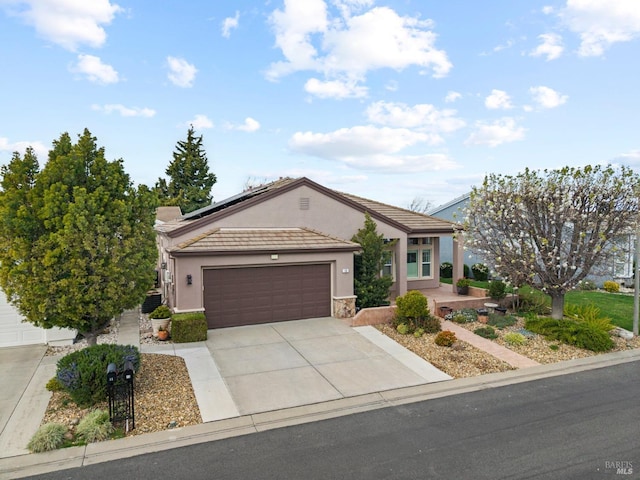 view of front of property featuring driveway, a garage, a tile roof, roof mounted solar panels, and stucco siding