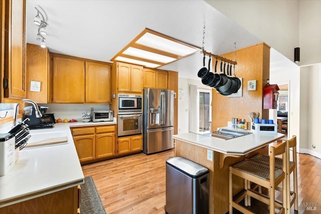 kitchen with a sink, light wood-type flooring, stainless steel appliances, light countertops, and a peninsula
