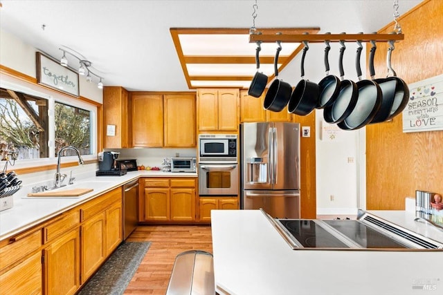 kitchen with stainless steel appliances, light wood-style flooring, a sink, brown cabinetry, and light countertops