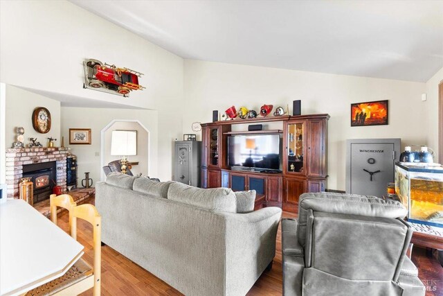 living room with vaulted ceiling, a brick fireplace, and wood finished floors