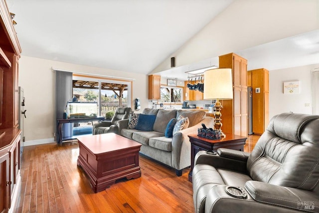 living area featuring baseboards, light wood-style flooring, and high vaulted ceiling