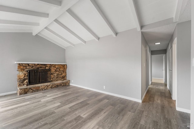 unfurnished living room featuring vaulted ceiling with beams, a stone fireplace, baseboards, and wood finished floors