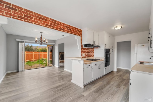 kitchen featuring light countertops, a chandelier, light wood-type flooring, oven, and under cabinet range hood