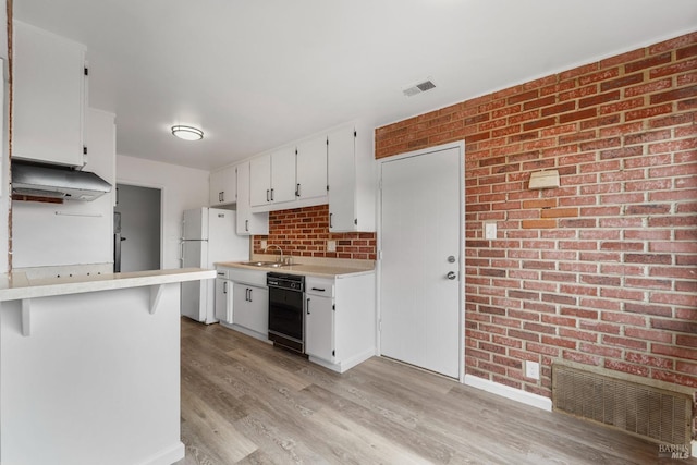 kitchen with black dishwasher, visible vents, freestanding refrigerator, a sink, and under cabinet range hood