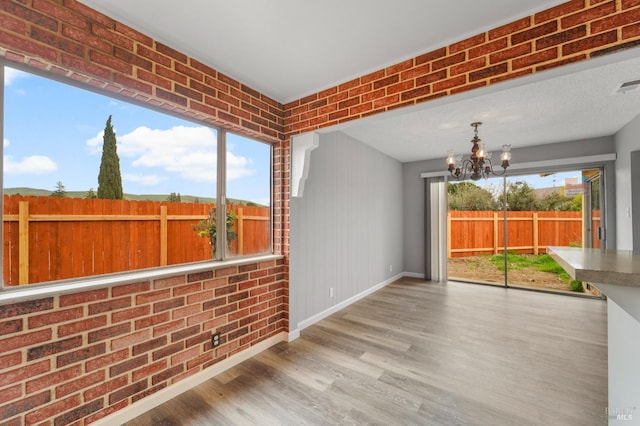 interior space with baseboards, brick wall, a chandelier, and wood finished floors