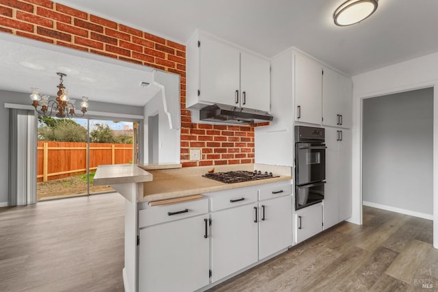 kitchen with a warming drawer, light countertops, light wood-style floors, under cabinet range hood, and black appliances