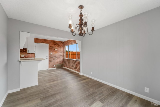 interior space with baseboards, brick wall, a chandelier, and wood finished floors