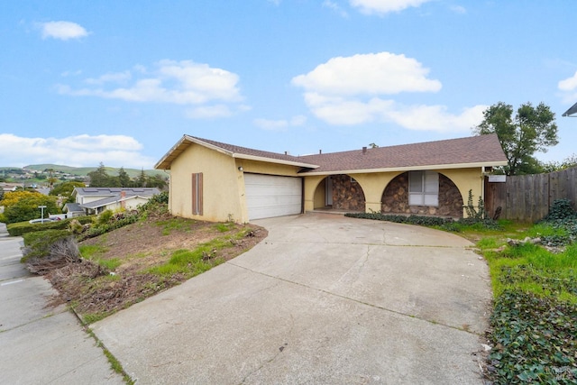 ranch-style house featuring an attached garage, fence, driveway, stone siding, and stucco siding