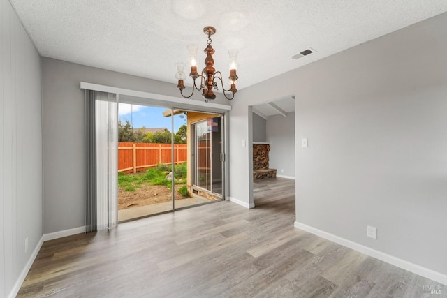 unfurnished dining area featuring visible vents, an inviting chandelier, a textured ceiling, wood finished floors, and baseboards