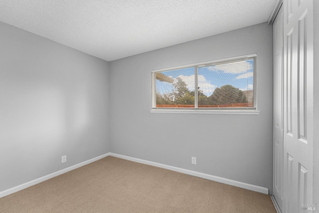 spare room featuring light carpet, a textured ceiling, and baseboards