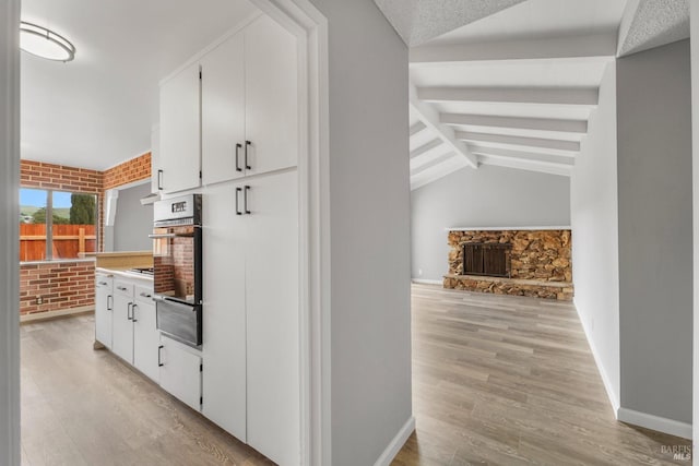 interior space with vaulted ceiling with beams, brick wall, light wood-style flooring, and baseboards