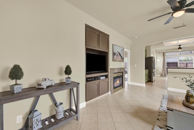 living area with light tile patterned floors, ceiling fan, visible vents, baseboards, and a glass covered fireplace