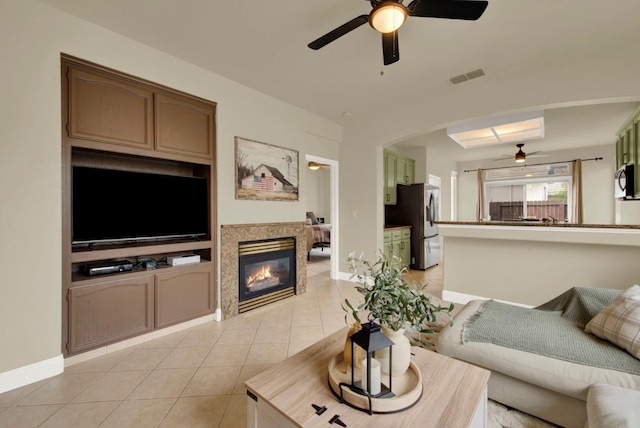 living room featuring light tile patterned floors, visible vents, a glass covered fireplace, ceiling fan, and baseboards