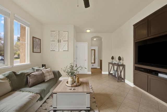 living area featuring arched walkways, light tile patterned flooring, a ceiling fan, and baseboards