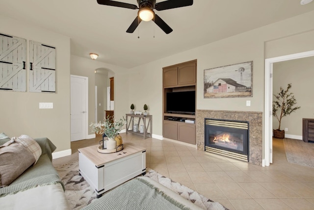 living room with arched walkways, light tile patterned floors, a ceiling fan, a glass covered fireplace, and baseboards