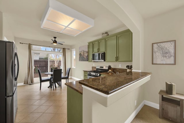 kitchen with light tile patterned flooring, stainless steel appliances, a peninsula, dark stone countertops, and green cabinetry