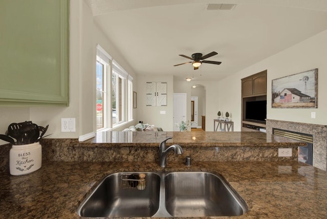 kitchen with arched walkways, visible vents, a sink, ceiling fan, and dark stone countertops