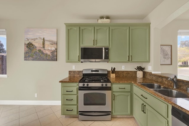 kitchen featuring light tile patterned floors, stainless steel appliances, green cabinets, a sink, and dark stone countertops