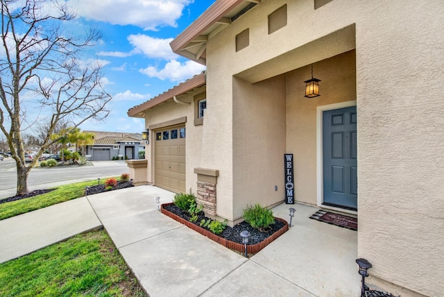 property entrance with a tile roof, stucco siding, a garage, stone siding, and driveway