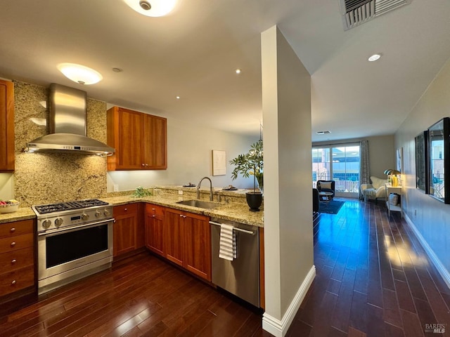 kitchen featuring brown cabinets, stainless steel appliances, visible vents, a sink, and wall chimney exhaust hood