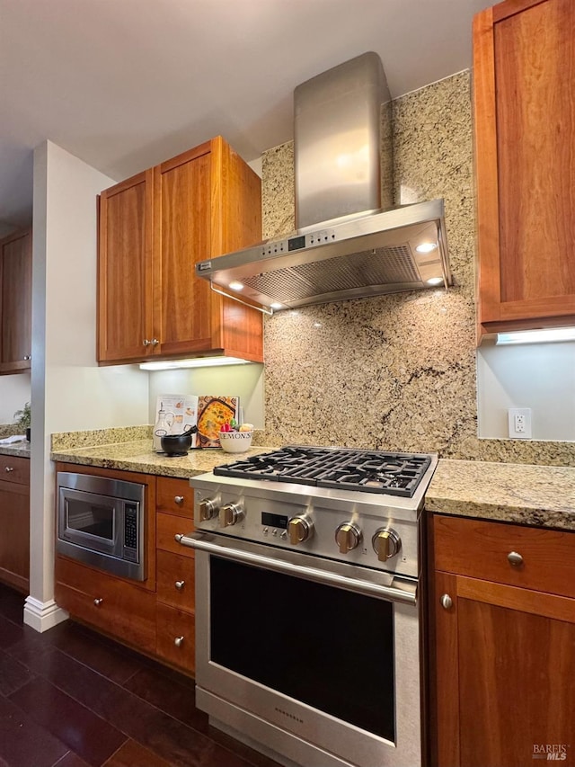 kitchen featuring light stone countertops, stainless steel appliances, brown cabinets, decorative backsplash, and wall chimney exhaust hood