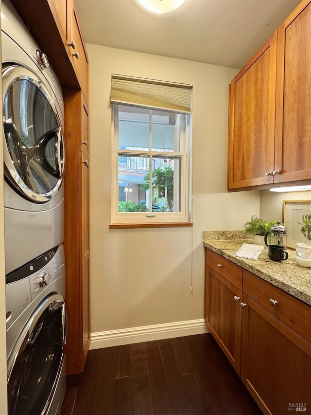 clothes washing area featuring baseboards, dark wood-type flooring, cabinet space, and stacked washer / drying machine