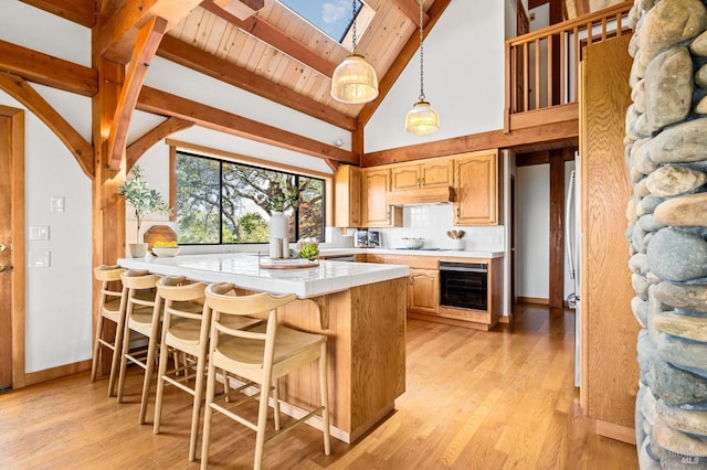 kitchen featuring a breakfast bar area, light wood-style flooring, under cabinet range hood, beam ceiling, and tile counters