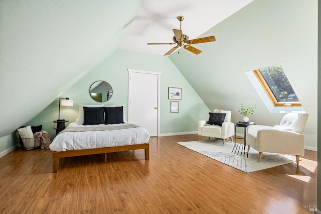 bedroom featuring vaulted ceiling with skylight, baseboards, and wood finished floors