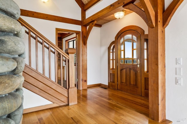 foyer entrance featuring arched walkways, stairway, wood finished floors, beamed ceiling, and baseboards