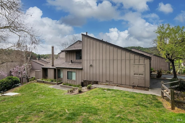 rear view of house featuring a lawn, board and batten siding, a shingled roof, and fence