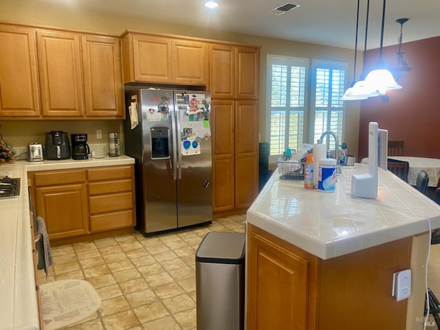 kitchen featuring visible vents, stainless steel refrigerator with ice dispenser, decorative light fixtures, a kitchen island, and tile counters