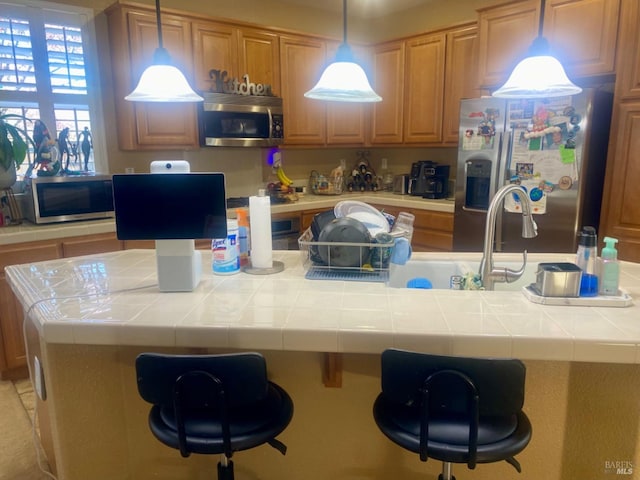 kitchen featuring decorative light fixtures, a breakfast bar area, appliances with stainless steel finishes, and tile counters