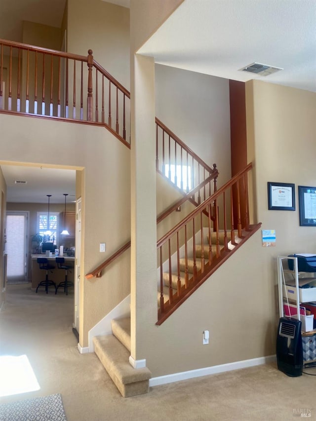 stairway with carpet flooring, baseboards, a high ceiling, and visible vents