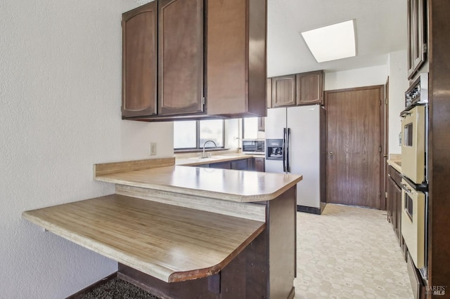 kitchen with a kitchen breakfast bar, stainless steel appliances, a peninsula, a skylight, and light countertops