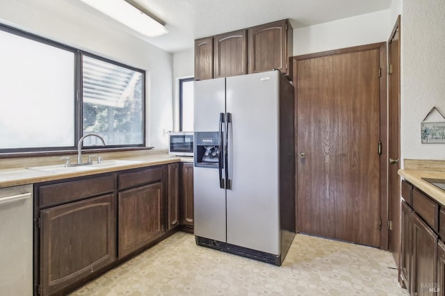 kitchen featuring light floors, a sink, light countertops, dark brown cabinetry, and appliances with stainless steel finishes