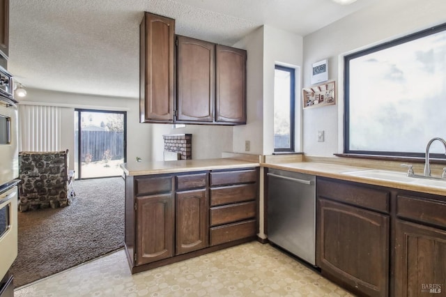 kitchen featuring a sink, stainless steel dishwasher, a textured ceiling, light countertops, and light colored carpet