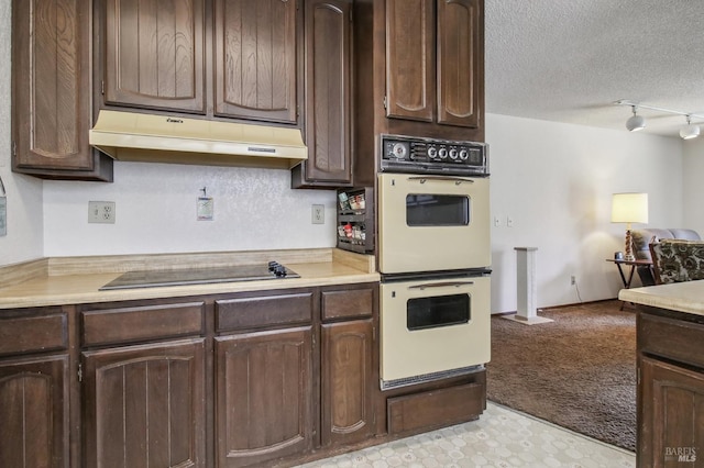 kitchen featuring dark brown cabinets, multiple ovens, under cabinet range hood, a textured ceiling, and black electric cooktop