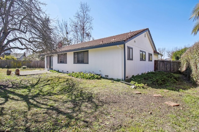 rear view of house with a tiled roof, a fenced backyard, a lawn, and crawl space