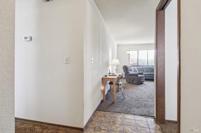 corridor featuring light colored carpet, baseboards, and a textured wall