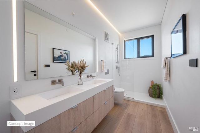 bathroom with wood finished floors, toilet, walk in shower, and a sink