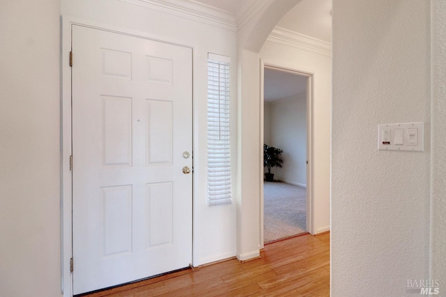 entrance foyer with arched walkways, a textured wall, baseboards, light wood finished floors, and crown molding